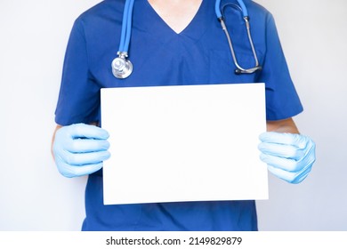 doctor dressed in blue uniform holds a white banner in his hands. Doctor card with stethoscope isolated on white background. mock up.