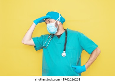 doctor dressed as a surgeon in green with stethoscope and mask on a yellow background with a worried expression.