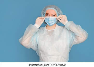 The doctor in a dressing gown, in medical gloves puts on a mask. Surgeon with clinical experience in healthcare, patient care. Copy space, isolated blue background.