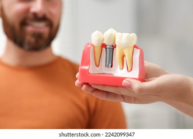 Doctor with educational model of dental implant consulting patient in clinic, closeup - Shutterstock ID 2242099347