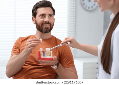 Doctor with educational model of dental implant consulting patient in clinic - Shutterstock ID 2281176507