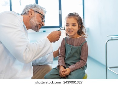 Doctor examining little girl's ear using otoscope, looking for ear infection. Friendly relationship between the doctor and the child patient. - Powered by Shutterstock