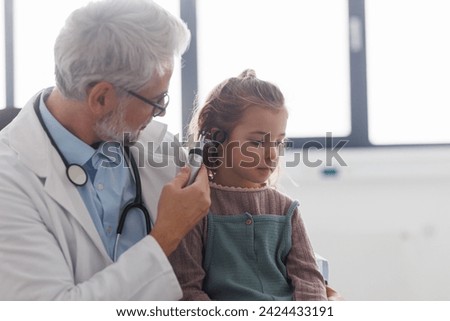 Doctor examining little girl's ear using otoscope, looking for infection. Friendly relationship between the doctor and the child patient.