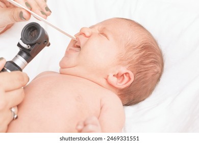 Doctor examining a newborn baby's mouth with an otoscope and tongue depressor in pediatric clinic - Powered by Shutterstock