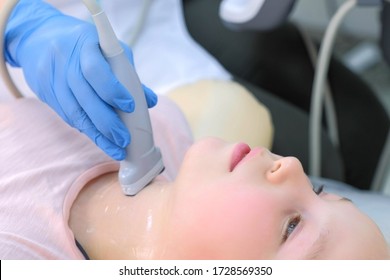 Doctor Examining Patient Child Girl Thyroid Gland Using Ultrasound Scanner Machine, Closeup View. Woman Runs Ultrasound Sensor Over Patient's Neck In Clinic. Diagnostic Examination.