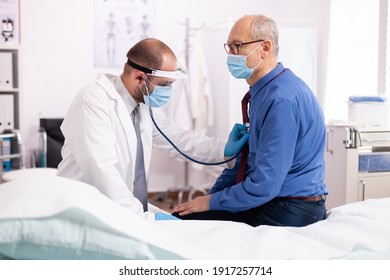 Doctor examining patient lungs using stethoscope wearing face mask as safety precaution in time of covid19. Medical practitioner wearing face mask consulting senior man in examination room during - Shutterstock ID 1917257714
