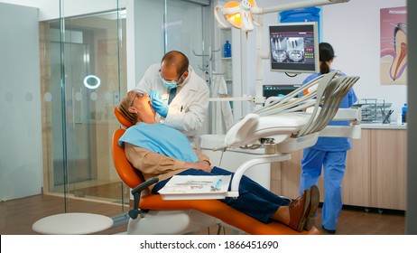 Doctor examining teeth with medical instruments working with gloves in modern dentist clinic. Orthodontist speaking to woman sitting on stomatological chair while nurse preparing tools for examination