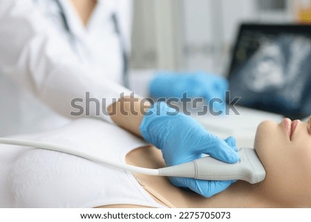 Doctor examining thyroid of female patient with ultrasound scan in clinic