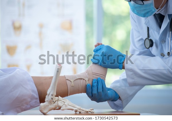 Doctor examining and training broken leg patient in\
hospital - physical therapy concept Orthopedic ankle doctor Doctor\
explains a patient bone structure of the legs using the layout of\
the foot 