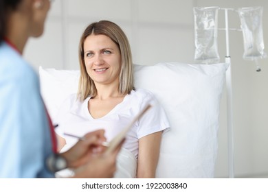 Doctor Examining Woman Lying On Bed In Hospital. Infusion Therapy Concept