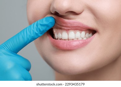 Doctor examining woman's gums on grey background, closeup