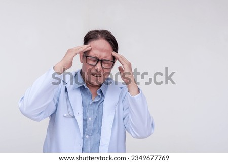 A doctor experiences an excruciating headache. Of asian descent, middle aged male. Isolated on a white background.