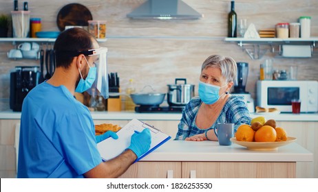 Doctor with face mask discussing about coronavirus pandemic with senior woman during home visit and taking notes. Male nurse social worker at retired senior couple visit explaining covid-19 spreading