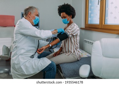 Doctor With Face Mask Measures Blood Pressure To The Patient At Hospital Office