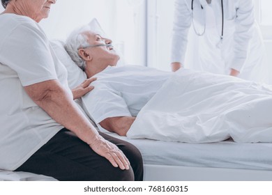 Doctor And Family Member Supporting Dying Senior Man Lying In Bed At The Hospital