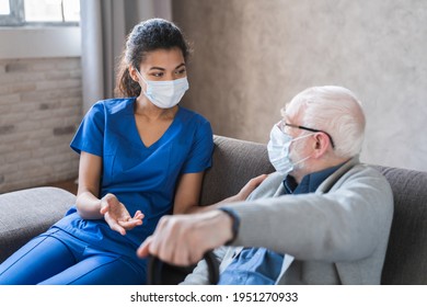 Doctor Or Female Caregiver With Senior Man Grandfather Wearing Protective Mask To Protect From Covid 19 At Home Or Nursing Home. Doctor Talking Consulting Elderly Patient At Home