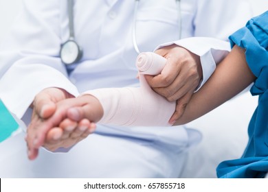 Doctor First Aid Child Patient's Arm Sprain With Elastic Bandage.