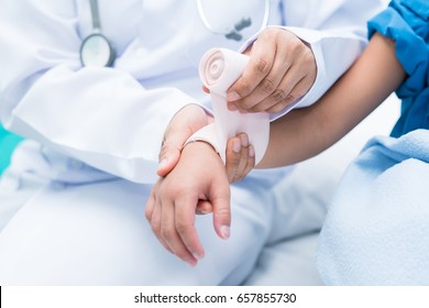 Doctor First Aid Child Patient's Arm Sprain With Elastic Bandage.