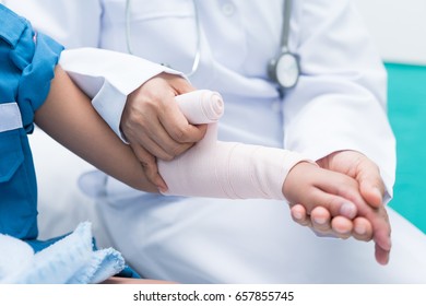 Doctor First Aid Child Patient's Arm Sprain With Elastic Bandage.