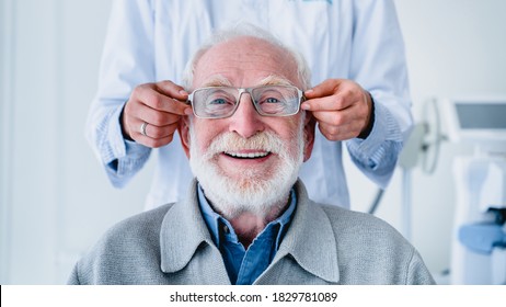 Doctor Fitting Glasses On Cheerful Aged Male Patient: Cropped Photo