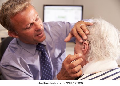Doctor Fitting Senior Female Patient With Hearing Aid