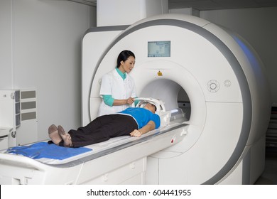 Doctor Fixing Mask To Patient Lying On CT Scan Machine