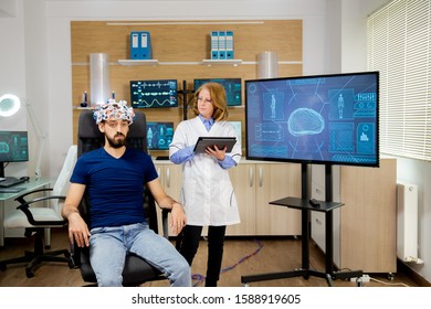 Doctor Following A Male Patient During Brain Scan Procedures. Brain Waves Scanning Helmet