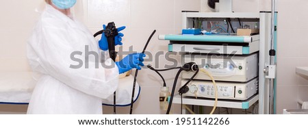 Doctor gastroenterologist in protective clothing holding endoscope before gastroscopy. Medical examination, medicine utensils and instruments, gastrointestinal fiberoptic endoscopy at modern hospital