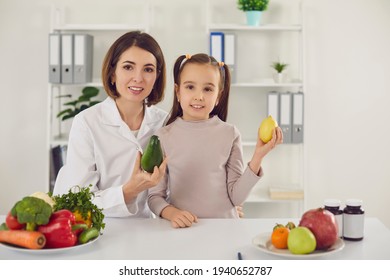 Doctor And Girl At Table With Fresh Raw Fruit, Vegetables And Vitamins. Dietitian Or Nutritionist With Little Child Teaching You To Eat Healthy Food And Maintain Nutritious Diet And Healthy Lifestyle