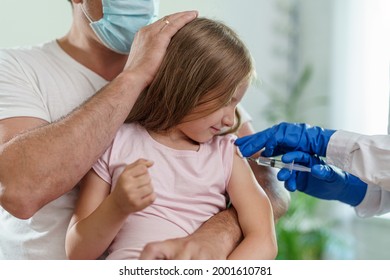 Doctor Gives A Brave Little Girl An Injection In The Shoulder. The Child Sits On Parent's Lap, Is Not Afraid And Smiles.Vaccination Of Children Against Coronavirus. Vaccine Against Covid-19. Close-up