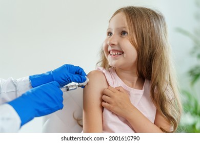 doctor gives a brave little girl an injection in shoulder. child is not afraid and smiles.Vaccination of children against coronavirus. vaccine against Covid-19. Close-up - Powered by Shutterstock