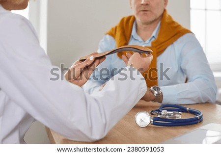 Doctor gives comfortable orthotic insoles to senior male patient. Woman podiatrist sitting at desk with mature man and holding orthopedic medical insole in her hands. Medicine, feet health concept