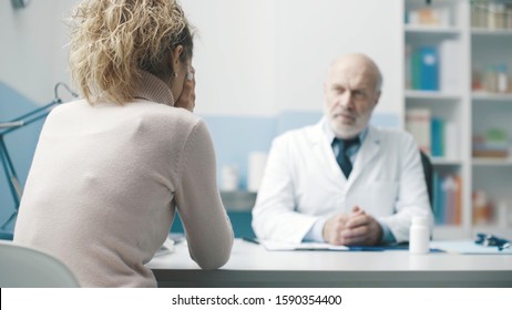 Doctor giving bad news to a patient, the woman is crying with head in hands