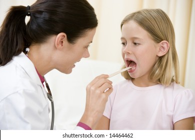 Doctor Giving Checkup To Young Girl With Tongue Depressor In Exam Room