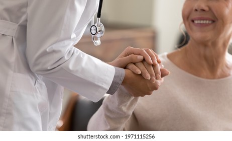 Doctor giving hope. Close up shot of young female physician leaning forward to smiling elderly lady patient holding her hand in palms. Woman caretaker in white coat supporting encouraging old person - Shutterstock ID 1971115256
