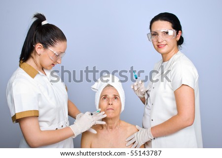 Doctor giving an injection to a senior woman cheek and the other doctor holding a syringe and smiling