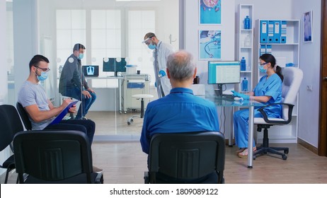 Doctor giving nurse patient radiography while finishing sick man examination in his office. Assistant with face mask against covid-19 pushing disabled woman in wheelchair through waiting area. - Powered by Shutterstock