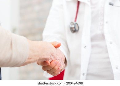 Doctor Giving Pensioner In Surgery Comfort And Consoling With Holding Hands 