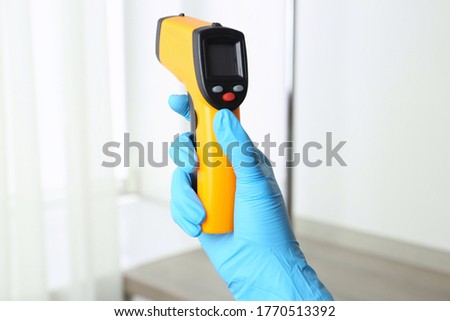 Doctor in gloves holding non contact infrared thermometer indoors, closeup
