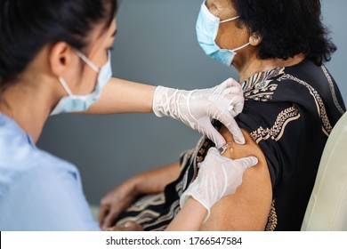 doctor in gloves holding syringe and making injection to senior patient in medical mask. Covid-19 or coronavirus vaccine - Shutterstock ID 1766547584