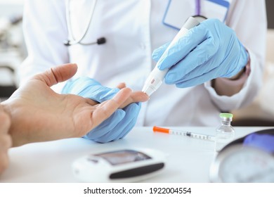 Doctor with gloves piercing patients finger with lancet closeup. Blood glucose monitoring concept