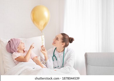 Doctor with golden balloon and little girl undergoing course of chemotherapy in clinic. Childhood cancer awareness concept