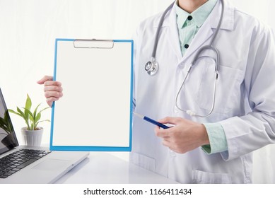 Doctor Hand Holding Pen And Pointing Blank Paper On Clipboard. Mockup For Health Care Information.