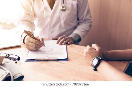 Doctor hand holding pen writing patient history list on note pad and talking to the patient about medication and treatment. - Powered by Shutterstock