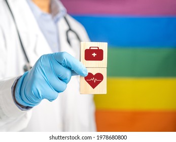 A Doctor Hand Holding Wooden Blocks With Icons Of Health Against The Background Of The Rainbow Flag (LGBT). Close-up Photo. Space For Text. Medical And Healthcare Concept.