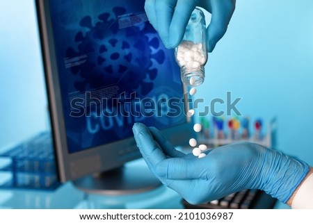 Doctor hand holds antiviral pills and background screen with illustration coronavirus covid-19 data. Researcher with oral pill bottle of pharmaceutical antiviral drugs against covid-19 coronavirus