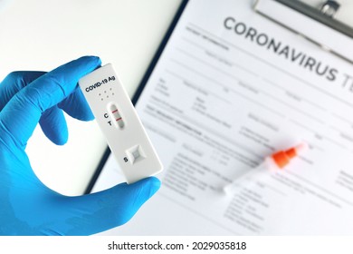Doctor hand showing covid-19 positive test on antigen rapid test kit for coronavirus with laboratory report on table.