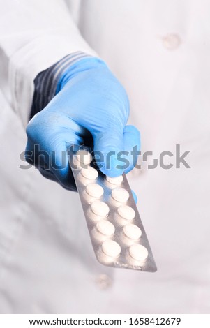 Doctor hand in sterile gloves holding blister pills close up view 