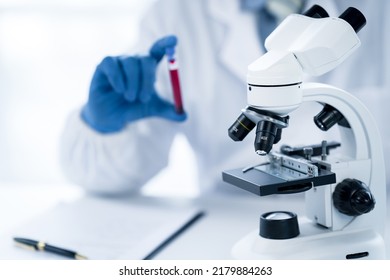 Doctor Hand Taking A Blood Sample Tube From A Rack With Machines Of Analysis In The Lab Background, Technician Holding Blood Tube Test In The Research Laboratory.