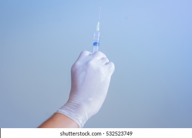 Doctor hand in white glove hold syringe with preparation jet from the needle. Medical man holding injector with drugs in arm. Surgeon with flu intravenous vaccine. Botox injection syringe therapy